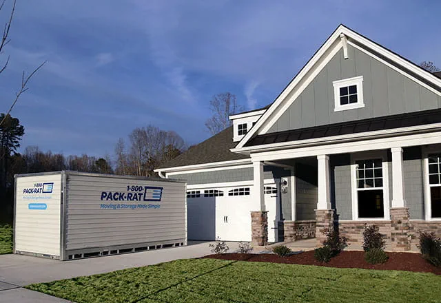 A 1-800-PACK-RAT container sits in the driveway of a new home, ready to be unpacked on a bright summer evening.